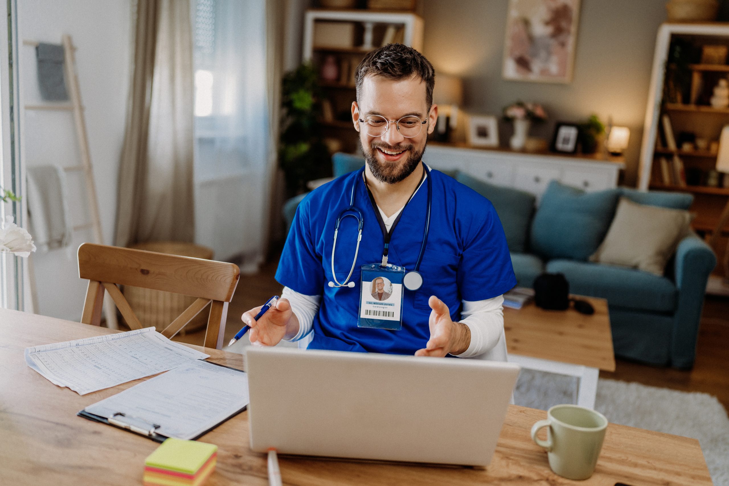 Remote physician assistant jobs. Male physician assistant in scrubs working in telehealth talking to a laptop.